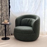 Dark green bouclé swivel barrel chair by sheer curtains and a floral drape, with a black side table