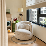 Oatmeal textured swivel barrel chair on a round rug beside a window in a bright room