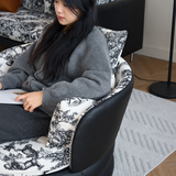 Woman seated in a barrel chair with black leather shell and toile cushions, holding paper