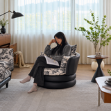 Woman reading in a black swivel barrel chair with toile cushions by sheer-curtained windows