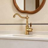 Vintage copper kitchen faucet with wood-grain handle and curved spout, set on a light marble countertop by a sink.