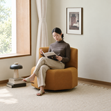 Tan swivel barrel chair with a seated woman reading beside a sunlit window