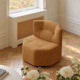 Tan textured barrel chair beside a window in a warm interior with foreground flowers