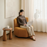 Tan swivel barrel chair in a sunlit room with a seated woman using a laptop