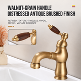 Antique brushed brass kitchen faucet with curved spout and walnut-grain lever handle, shown on a white basin beside a vase