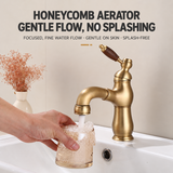 Antique brass bathroom faucet with wood-grain handle running water into a glass held under the spout at a white sink.
