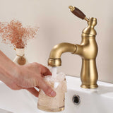 Antique brass faucet with wood-grain handle filling a glass at a white sink