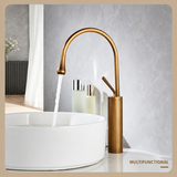 Antique brushed brass kitchen faucet with a high-arc spout pouring water into a white vessel sink, two bottles beside it.
