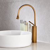 Vintage kitchen faucet in antique brushed brass above a round white vessel sink, with two bottles in soft colors beside it.