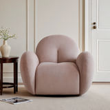 Dusty pink velvet swivel barrel chair in a cream paneled room with dark wood side table, vase and magazine