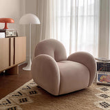 Blush pink velvet swivel barrel chair on a patterned rug beside a wood cabinet and white floor lamp, sheer curtains behind.