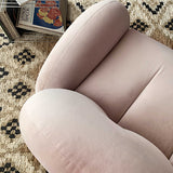 Overhead close-up of blush pink velvet barrel chair seat and rounded arm on a patterned rug, magazines stacked nearby.