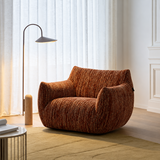 Rust-brown textured swivel barrel chair in a bright living room with white curtains and an arc floor lamp