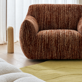 Rust-brown ribbed chenille swivel chair arm and seat, sheer curtains, wood floor