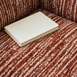 Close-up of a rust-brown and cream striped chenille chair seat and backrest with a plain cream book resting on the cushion