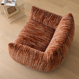 Rust-brown textured swivel barrel chair seen from above on light wood flooring, beside a wire magazine rack